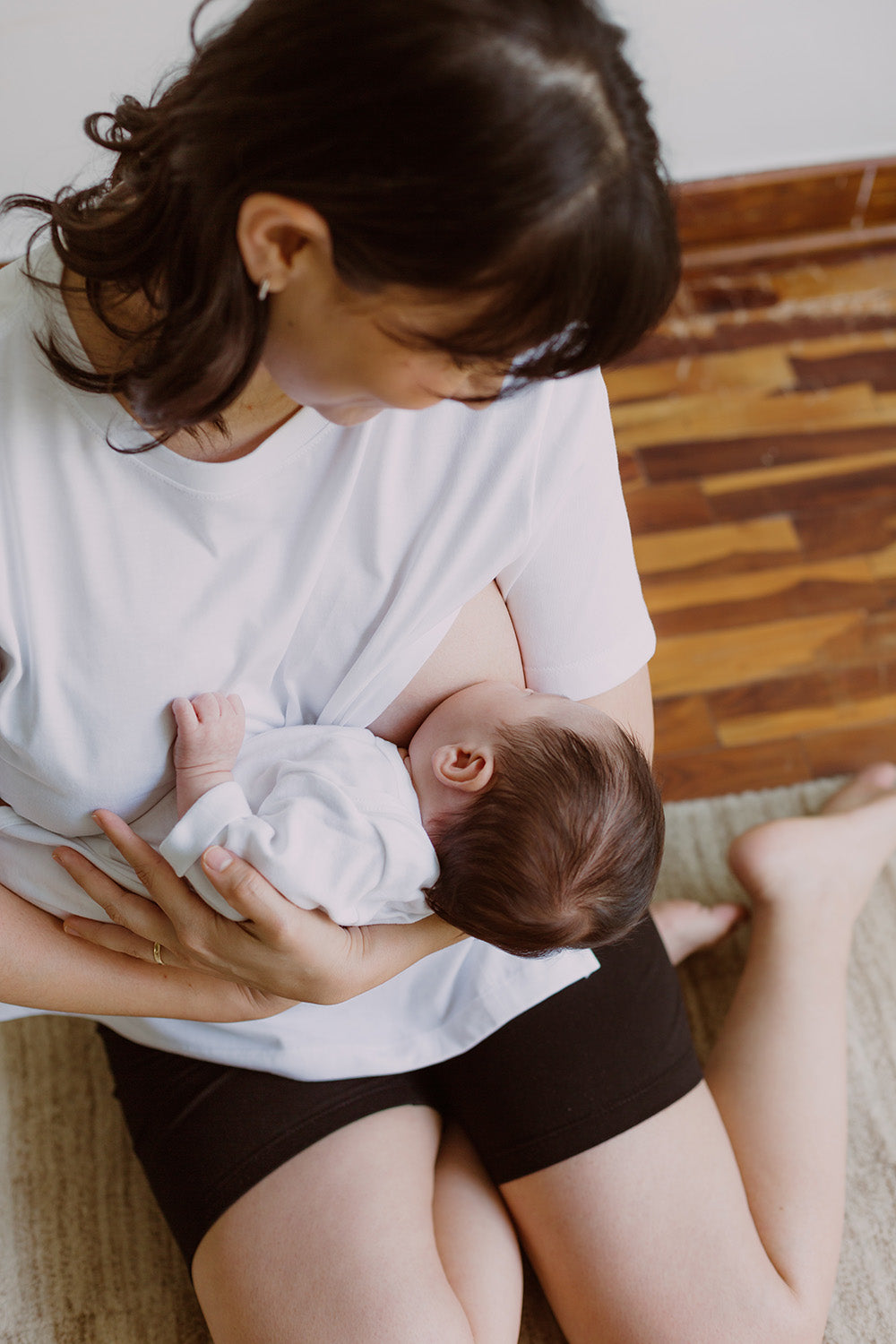 Mujer usando un polo básico color blanco. En sus brazos sujeta a un bebe al que le está dando de lactar.