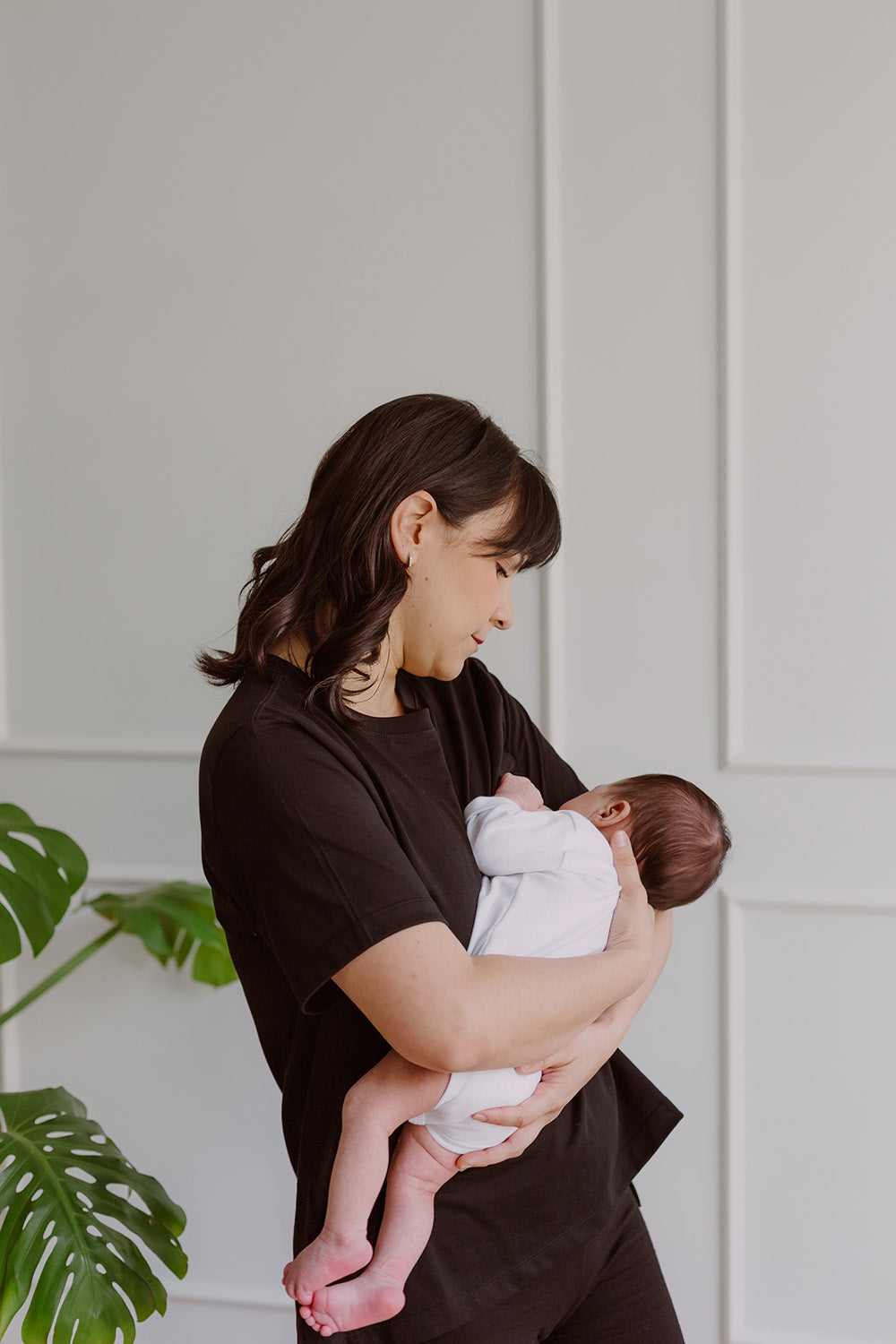 Mujer usando un polo básico color negro. En sus brazos carga a un bebe al que le está dando de lactar.