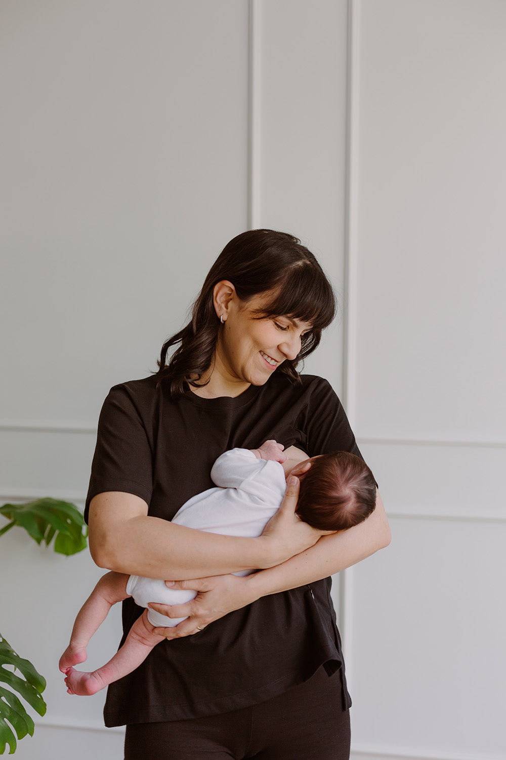 Mujer usando un polo básico color negro. En sus brazos carga a un bebe al que le está dando de lactar.