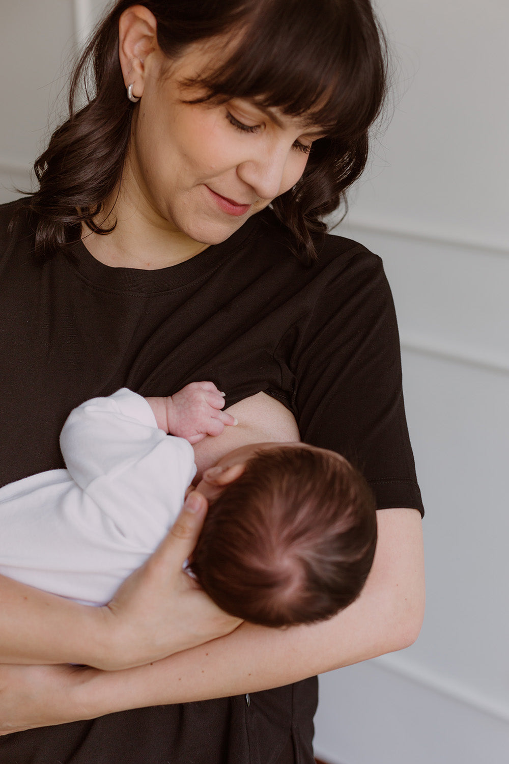 Mujer usando un polo básico color negro. En sus brazos carga a un bebe al que le está dando de lactar.