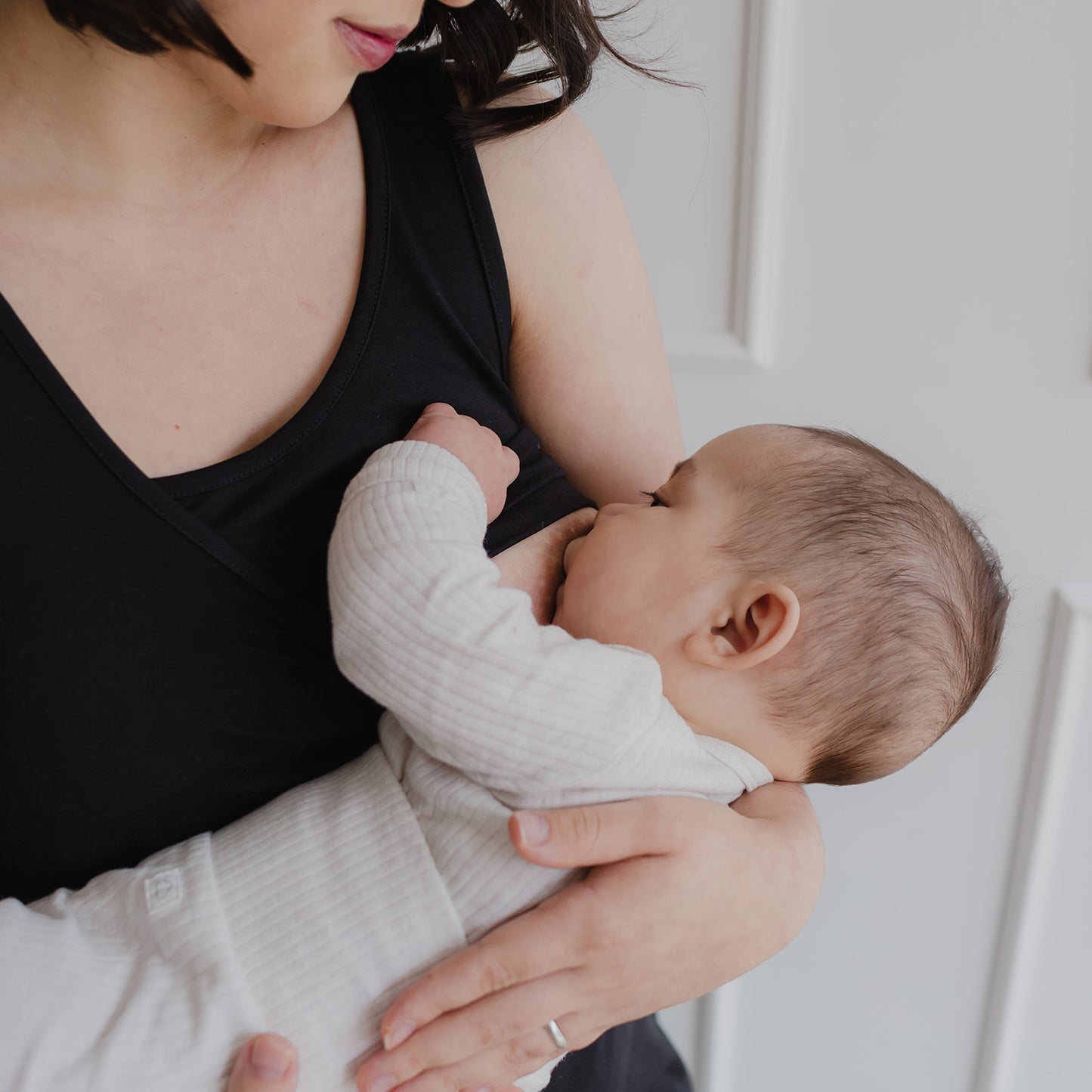 Mujer usando un vestido negro. En sus brazos sostiene a un bebe al cual le da de lactar.