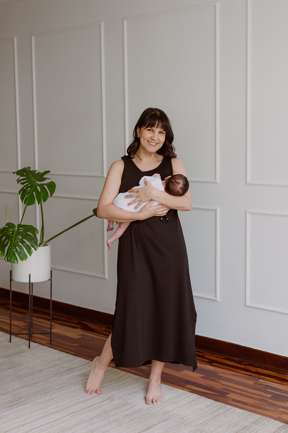 Mujer usando un vestido negro. En sus brazos sostiene a un bebe al cual le da de lactar.