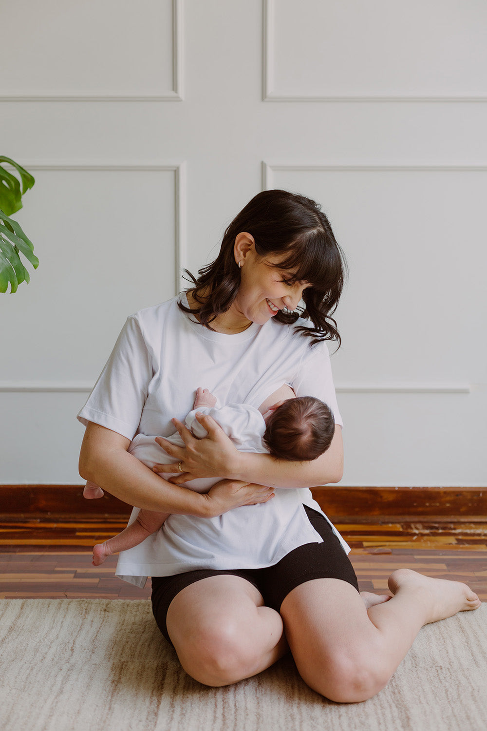 Mujer usando un polo básico color blanco. En sus brazos sujeta a un bebe.