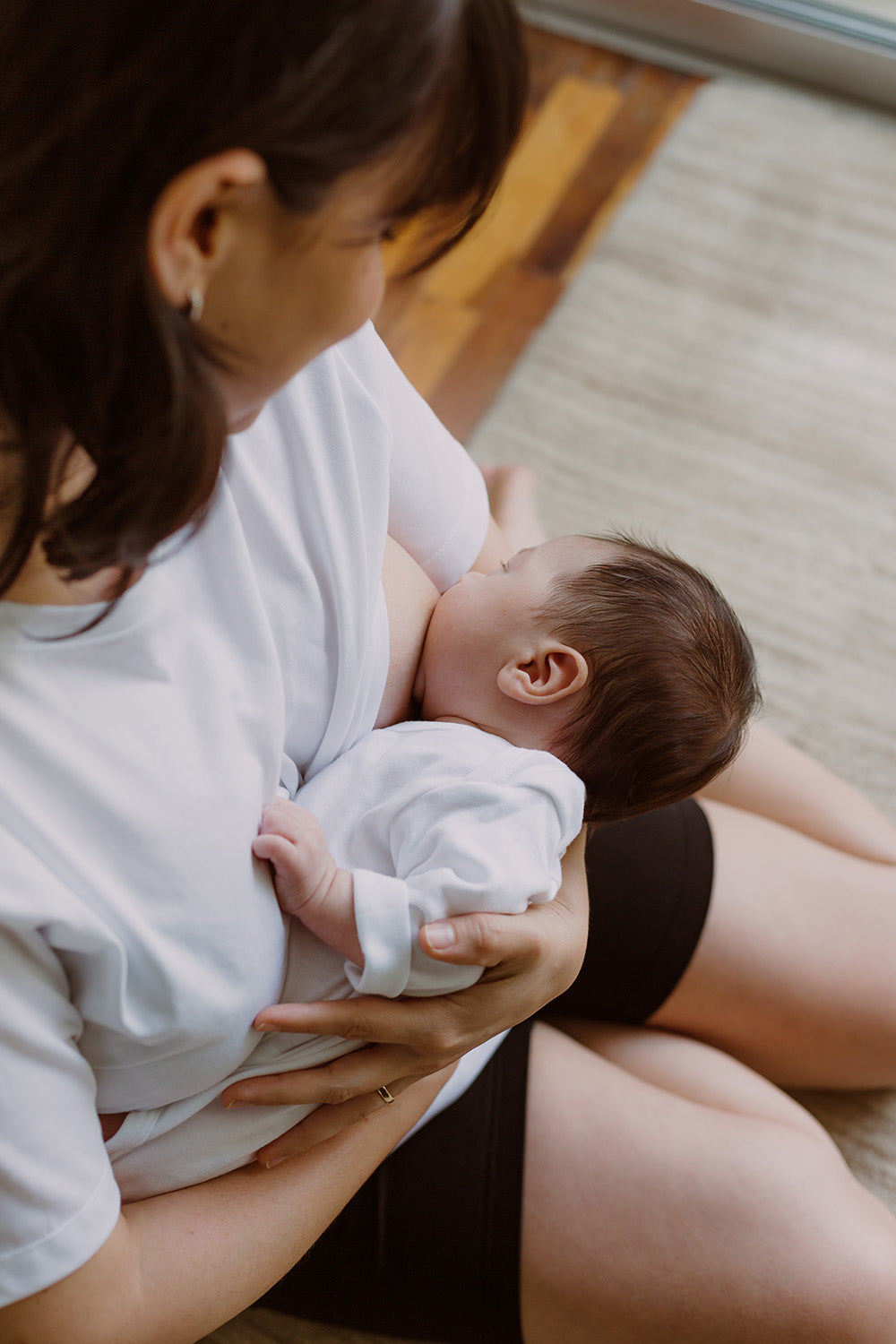 Mujer usando un polo básico color blanco. En sus brazos sujeta a un bebe al que le está dando de lactar.