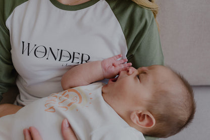 Mujer  usando un polo manga larga de color blanco y verde. En sus brazos carga a un bebe.