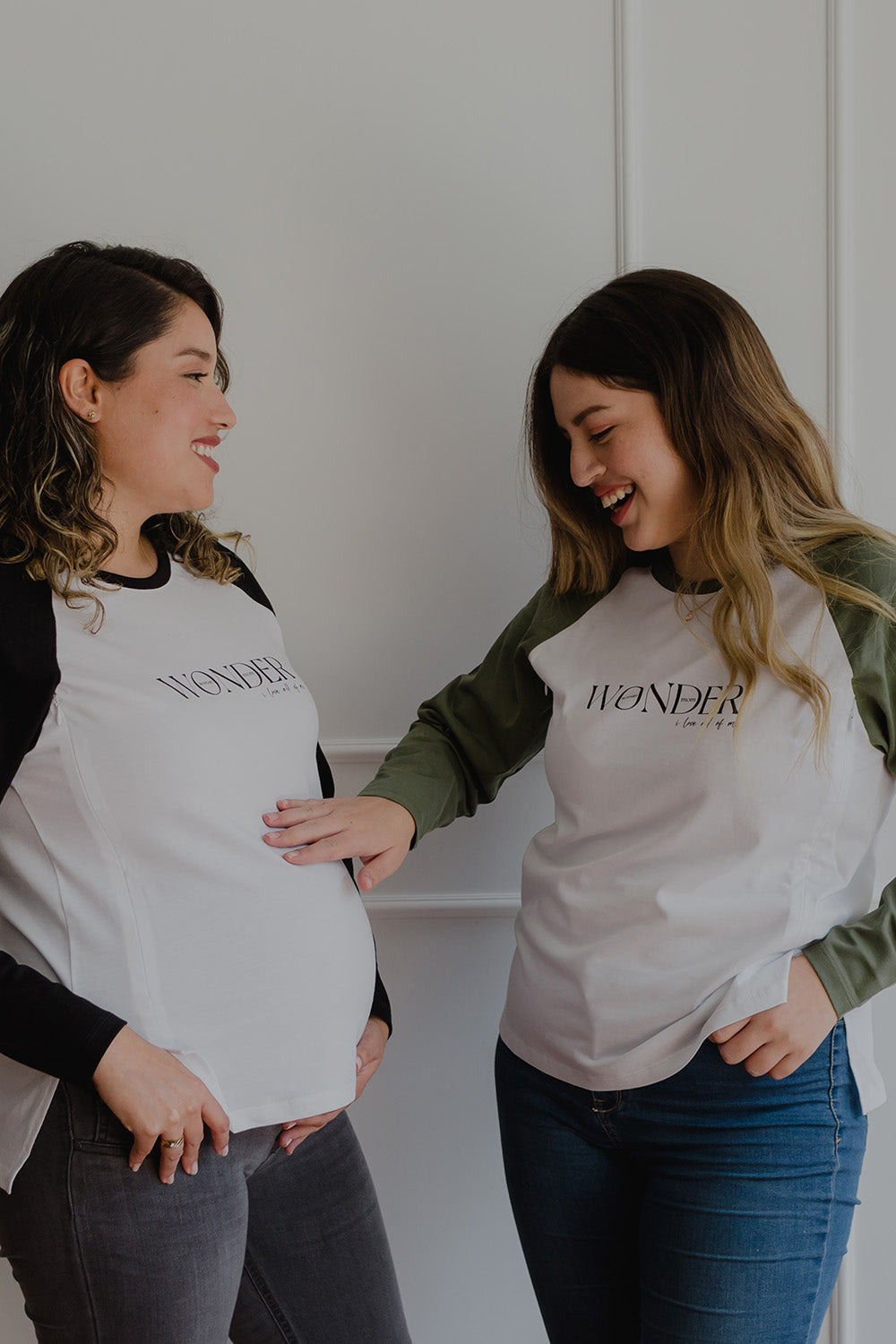 Dos mujeres usando un polo manga larga de color verde y blanco.  Una de ellas está embarazada.
