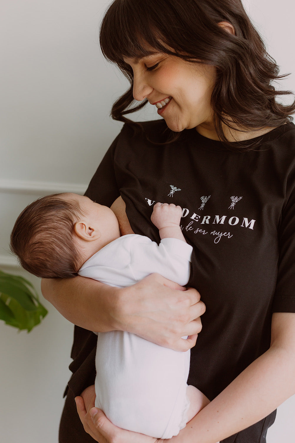 Mujer usando un polo negro. En sus brazos carga a un bebe al que le está dando de lactar.