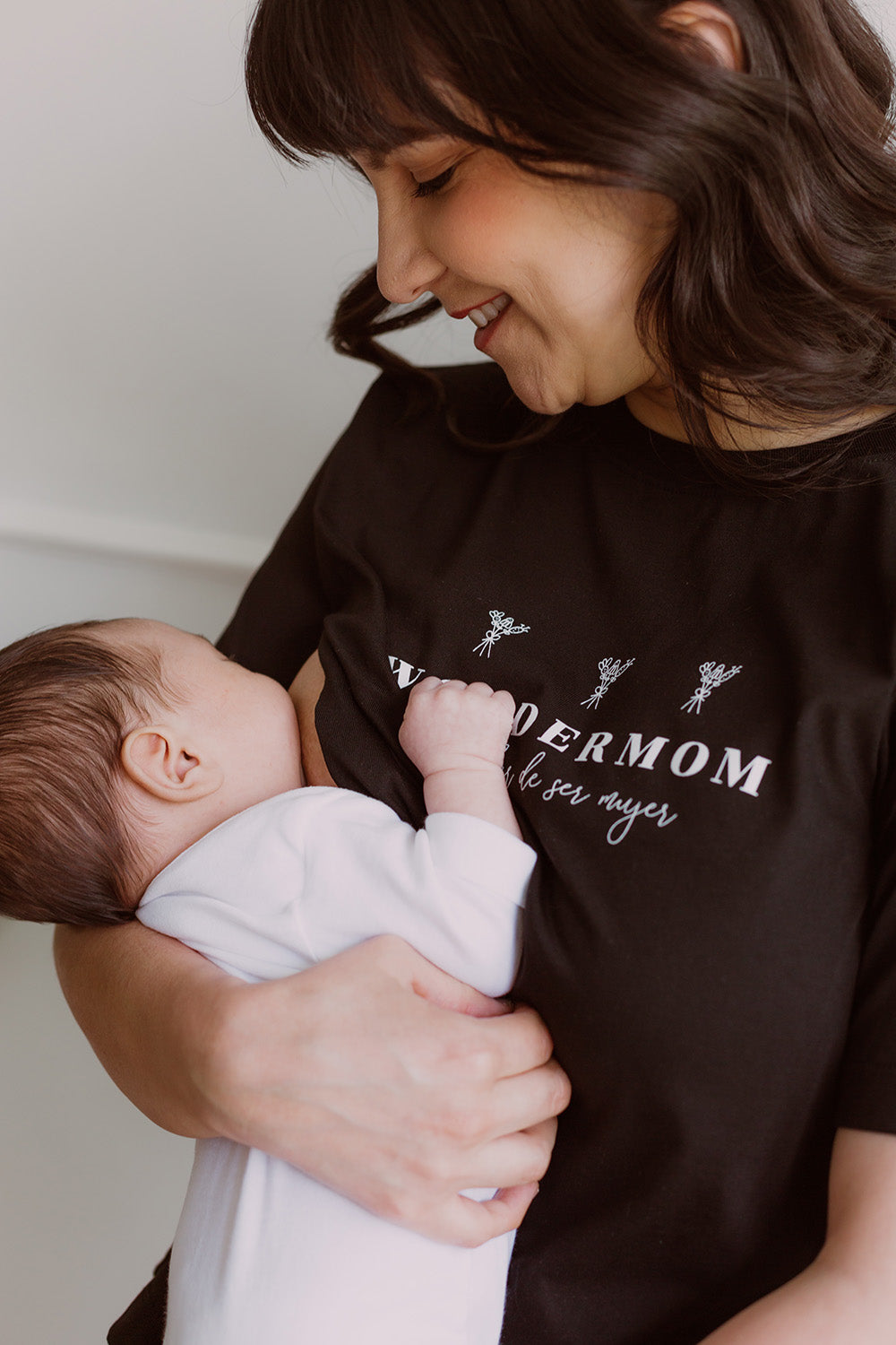 Mujer usando un polo negro. En sus brazos carga a un bebe al que le está dando de lactar.