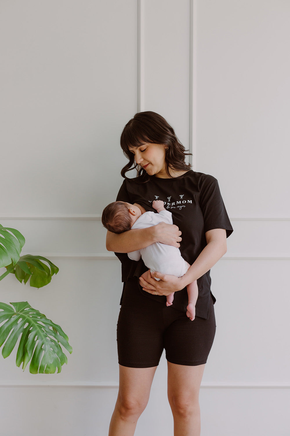 Mujer usando un polo negro. En sus brazos carga a un bebe al que le está dando de lactar.