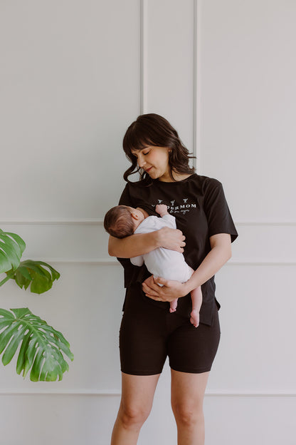 Mujer usando un polo negro. En sus brazos carga a un bebe al que le está dando de lactar.