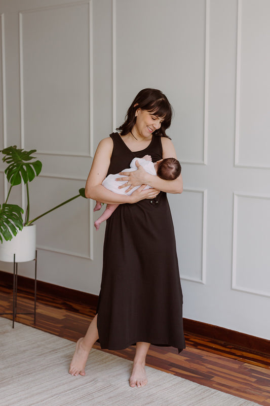 Mujer usando un vestido negro. En sus brazos sostiene a un bebe al cual le da de lactar.